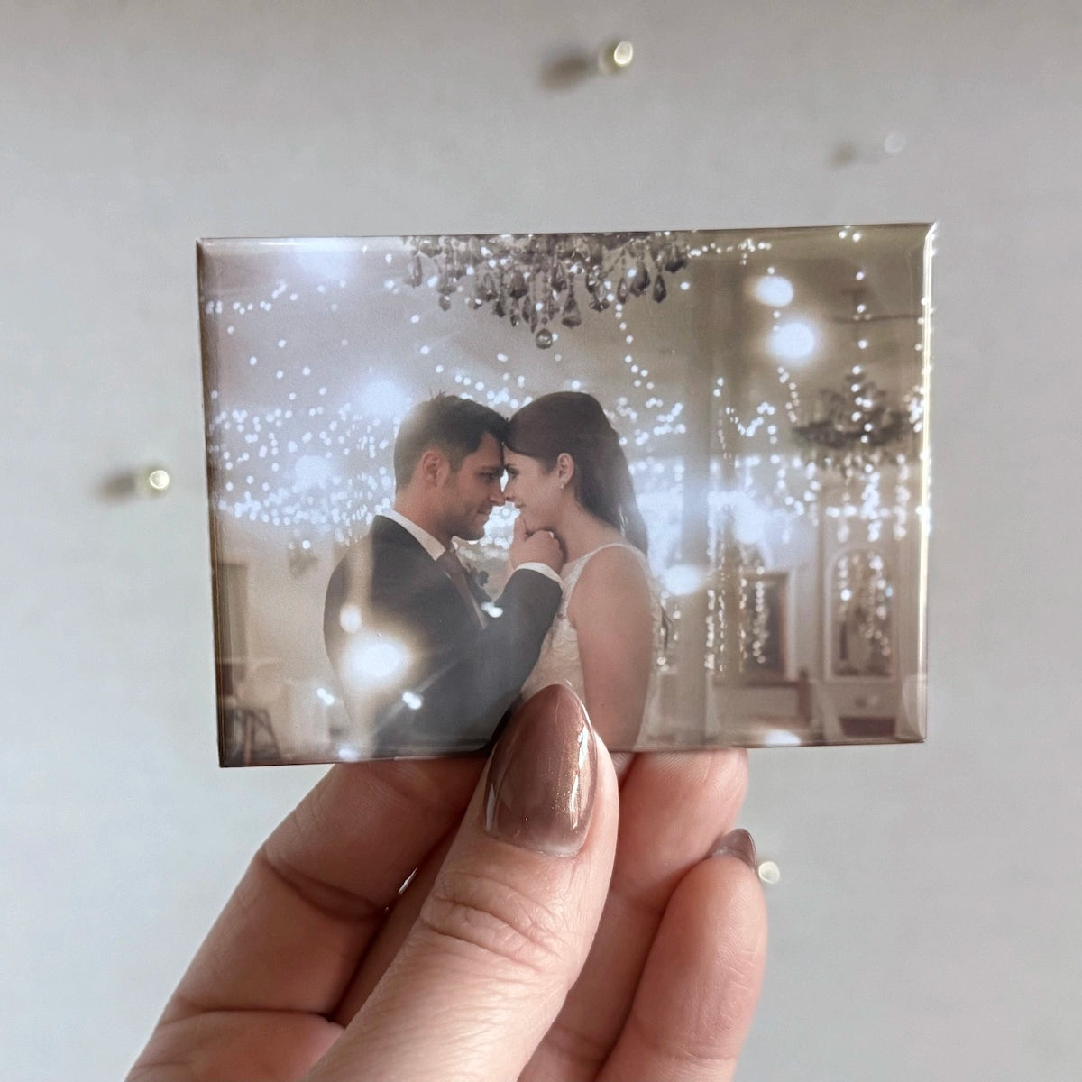 Custom photo magnet showcasing a romantic wedding portrait of a bride and groom under chandelier lights and dreamy bokeh sparkle. A timeless wedding keepsake, turned into a glossy magnetic photo souvenir for your fridge or gift box. Elegant, emotional, and made to last.